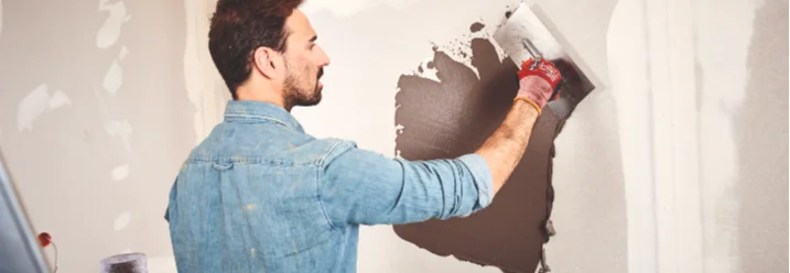 Person trägt mit einer Glättkelle Spachtelmasse auf eine Trockenbauwand im Innenbereich auf